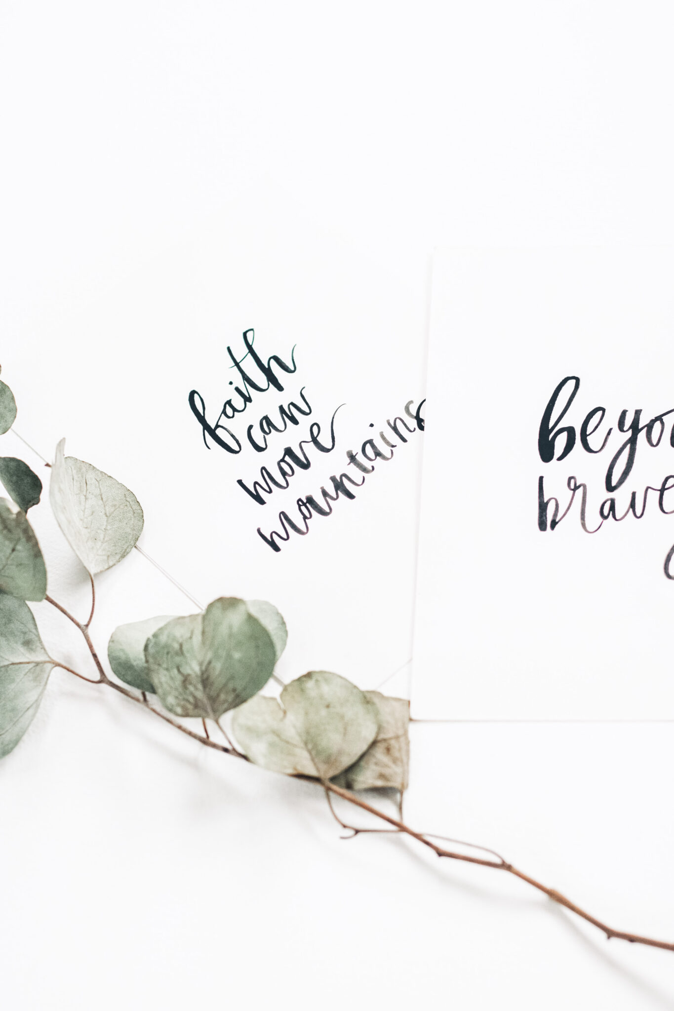 Two black and white faith-inspired posters written in cursive. On the side is a sprig of eucalyptus.  This article covers practical ways to encourage your kids to develop faith.