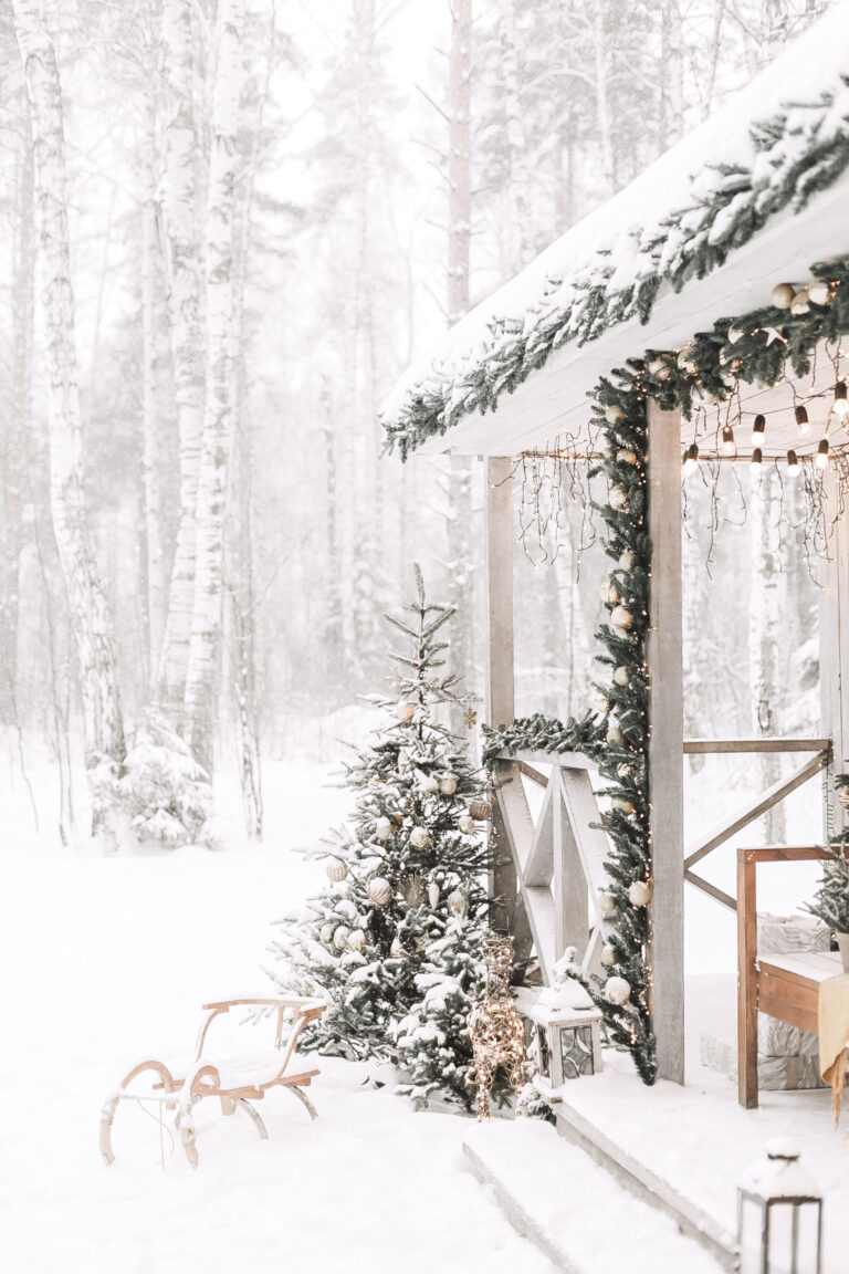 A beautiful front porch decorated from Christmas is shown against a beautiful winterscape. This article covers tips to get your house ready for winter.