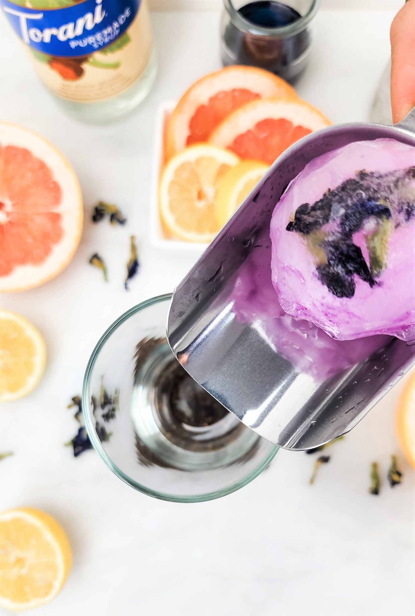 A lemon and butterfly pea tea infused ice ball is being placed into a glass.