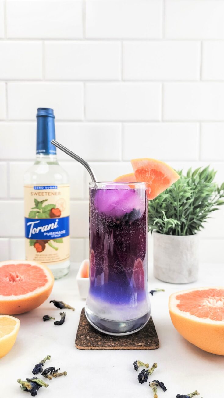 A tall glass shows a glittering drink that is layered and ombre. It is white on the bottom, then purple, then red. It's a color changing Hibiscus Tea Galaxy Refresher