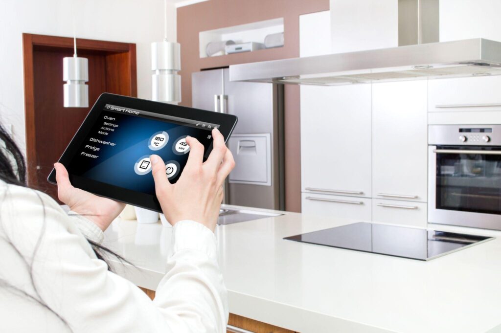 Hands hold a tablet and control appliances in the kitchen. 