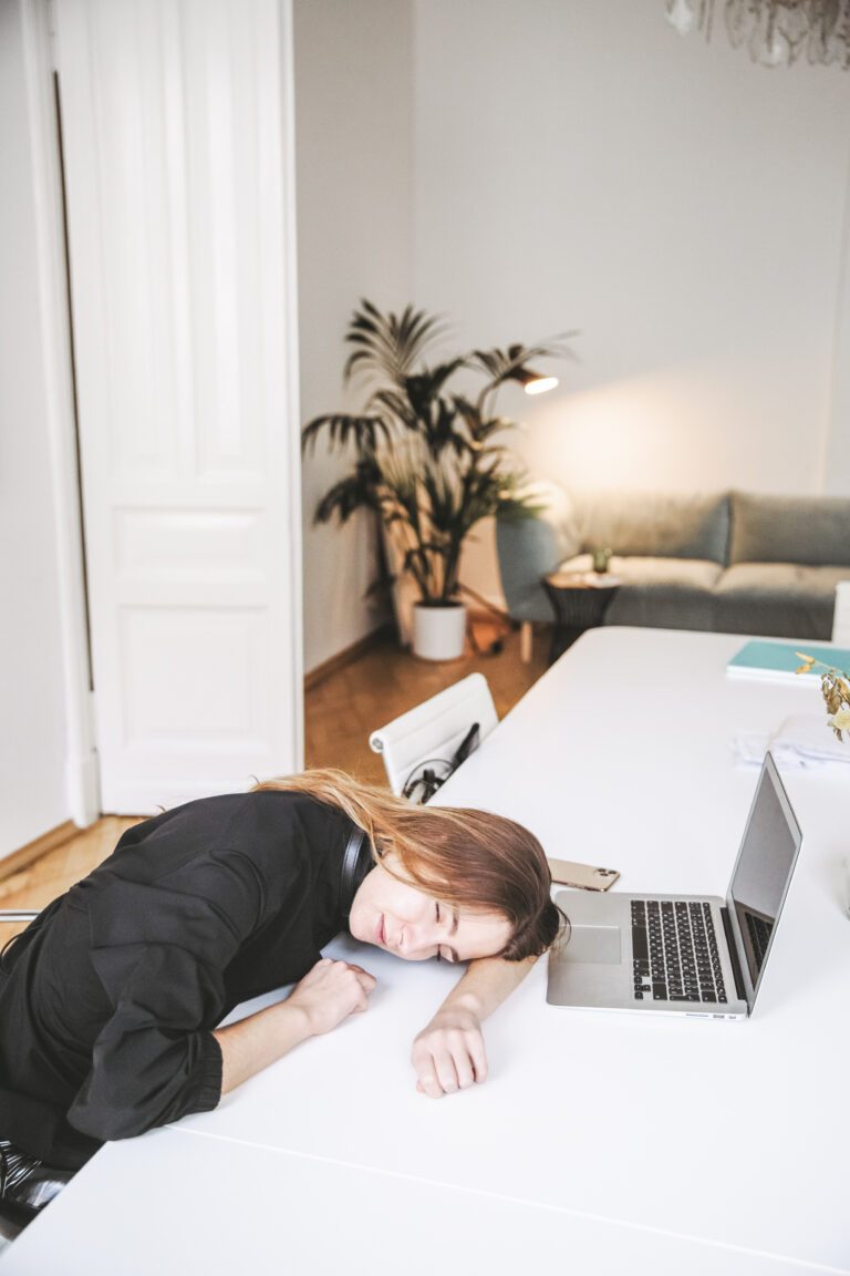 Woman drained of energy lays her head on her desk near her laptop. She is in a home office. This article covers how to schedule a creativity reset.