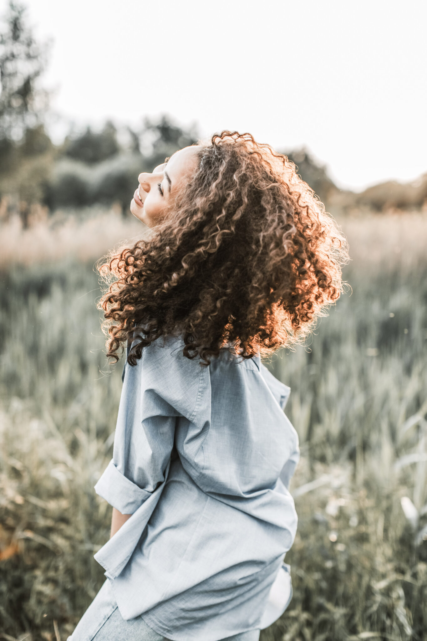 A woman with curly hair joyfully spins in a beautiful trail outside. This post covers 4 essential summer stress relief tips.