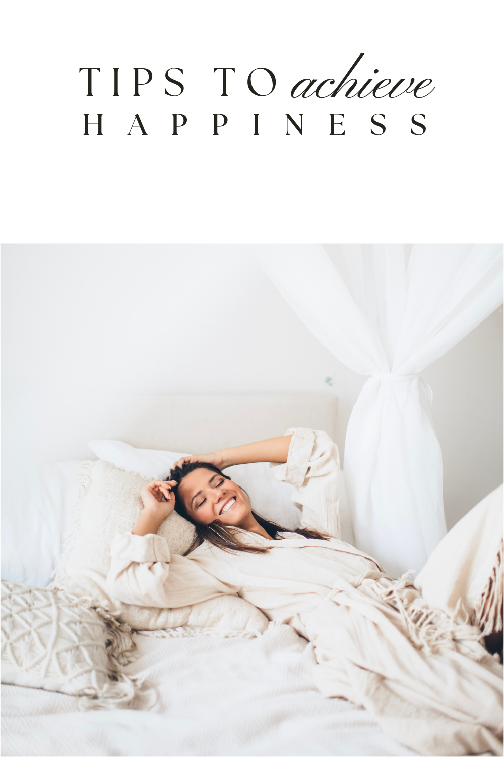 A woman lies in her bed on white sheets, she is wearing neutral pajamas and is closing her eyes and smiling. This article covers tips to achieve happiness. 