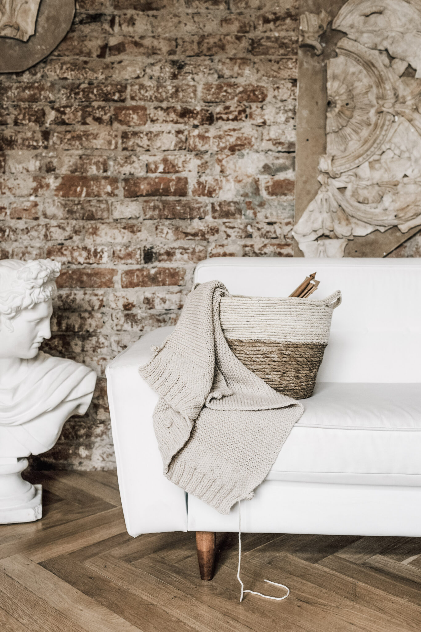A beautiful white couch with a basket with yarning needles and yarn. This picture depicts the inside of an apartment. This article covers the most important summer maintenance tasks for landlords.