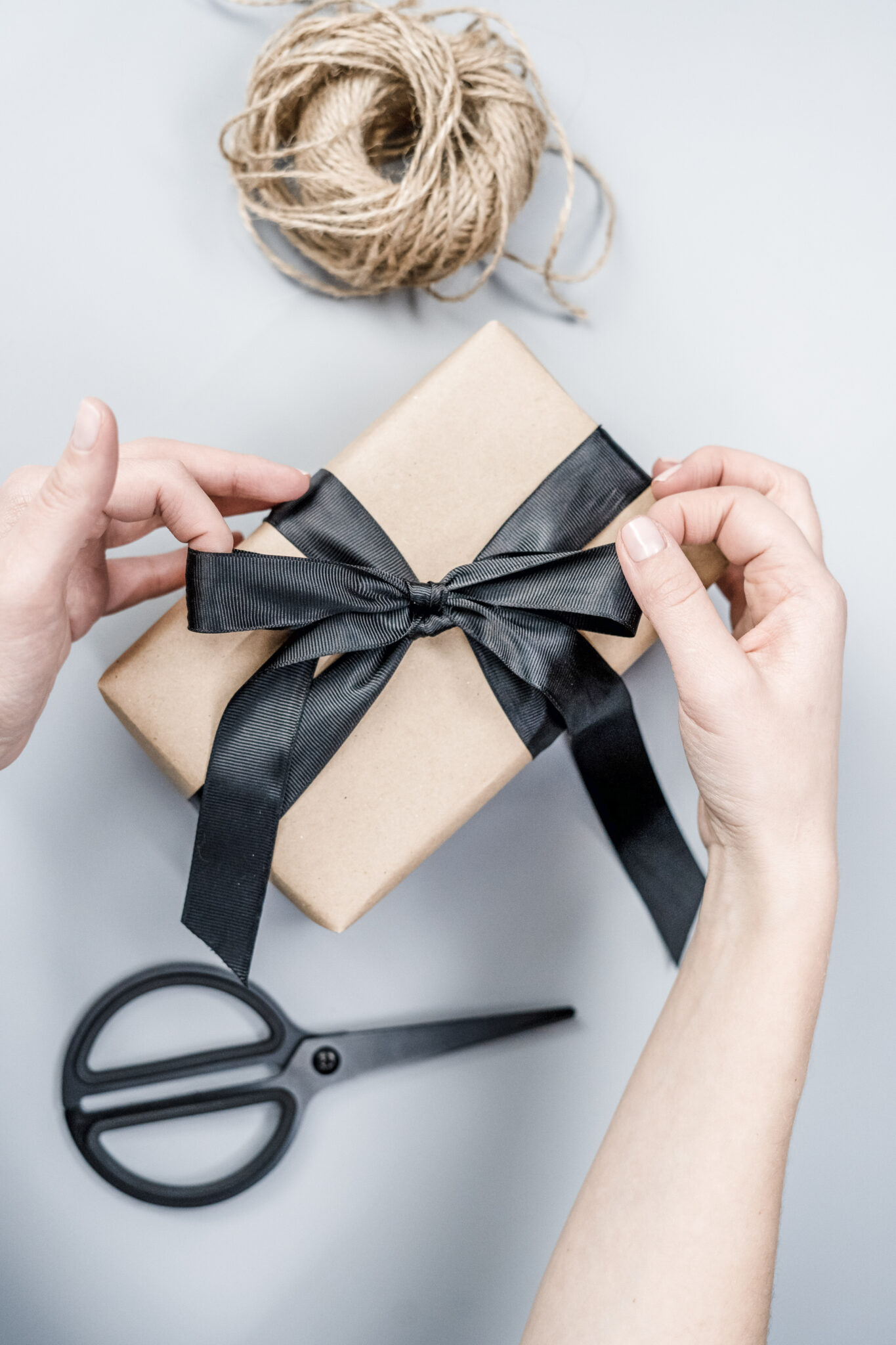 A woman wraps a present with butcher paper, black ribbon, and rope. This article covers tips to pick the right Birthday hampers for your co-worker.
