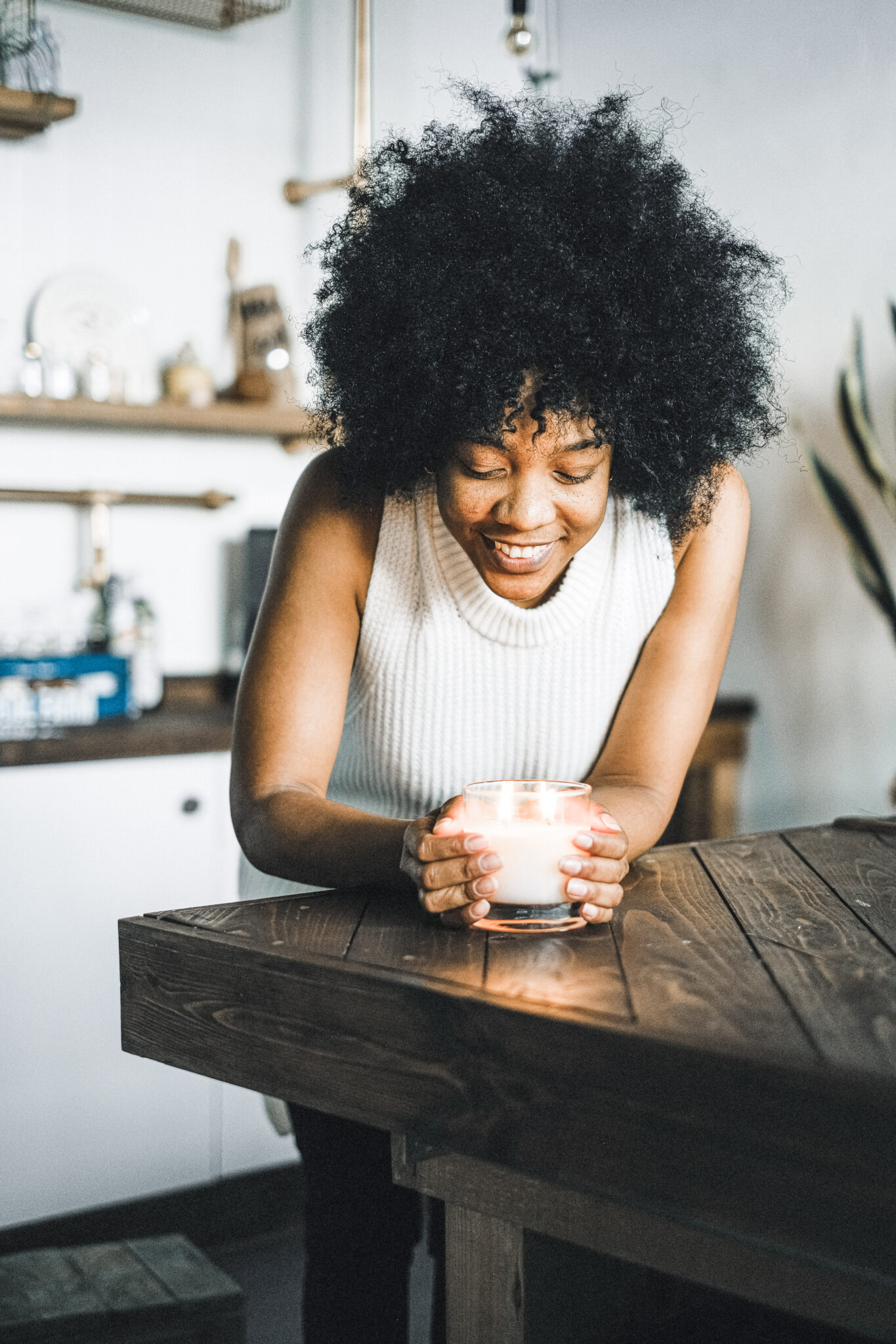 Woman holds a lit candle in the kitchen table. She smiles and is happy. This article covers ways to feel happier in your home.
