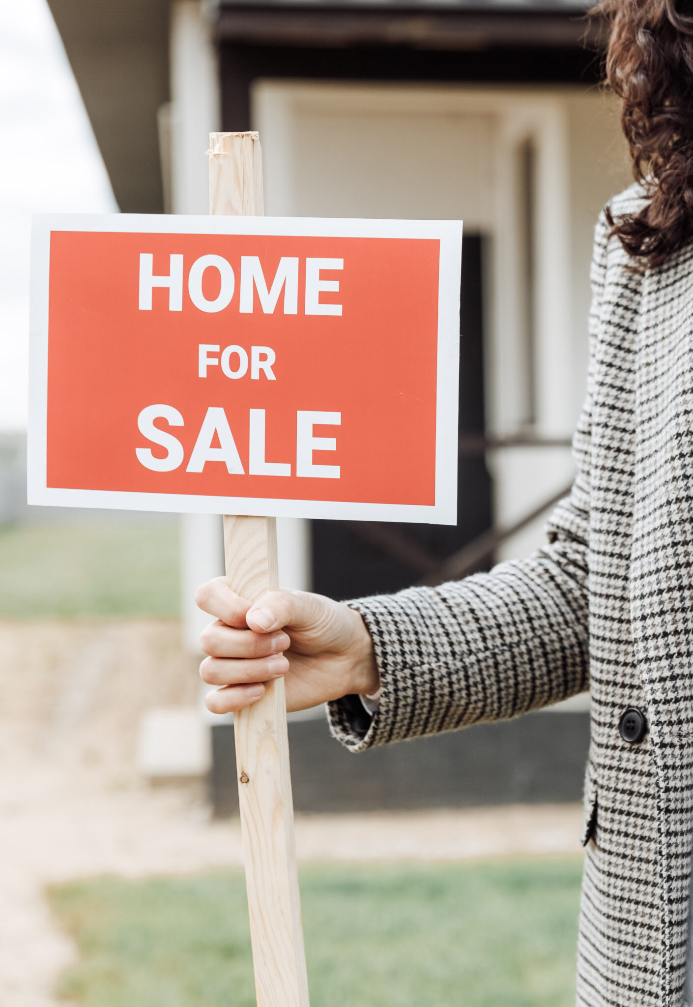 A female realtor holds a Home for Sale sign. This article covers 3 things standing in the way of your home selling.