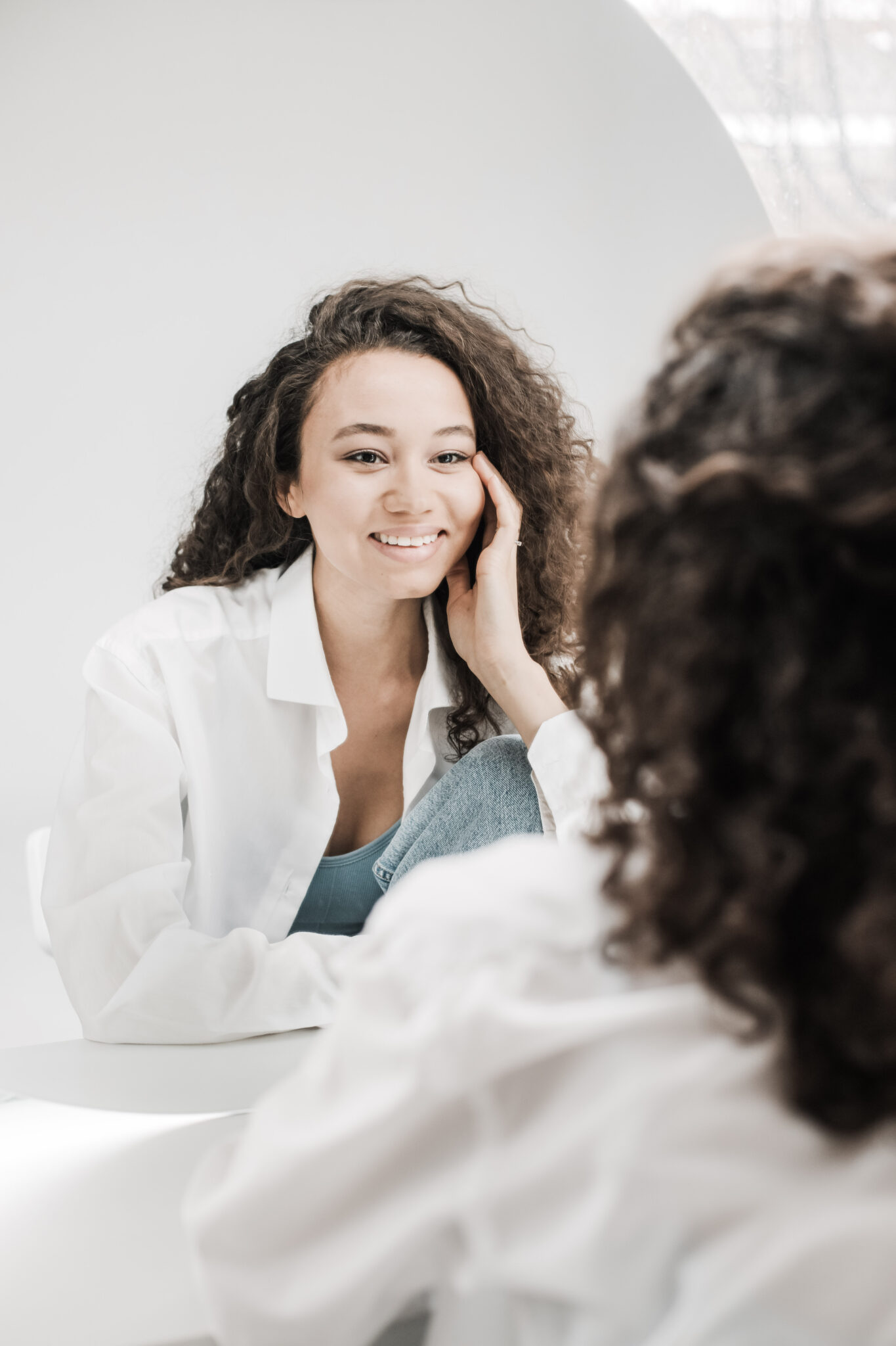 A beautiful curly-haired woman looks in the mirror at her reflection and smiles. This article covers the best confidence boosters for women.
