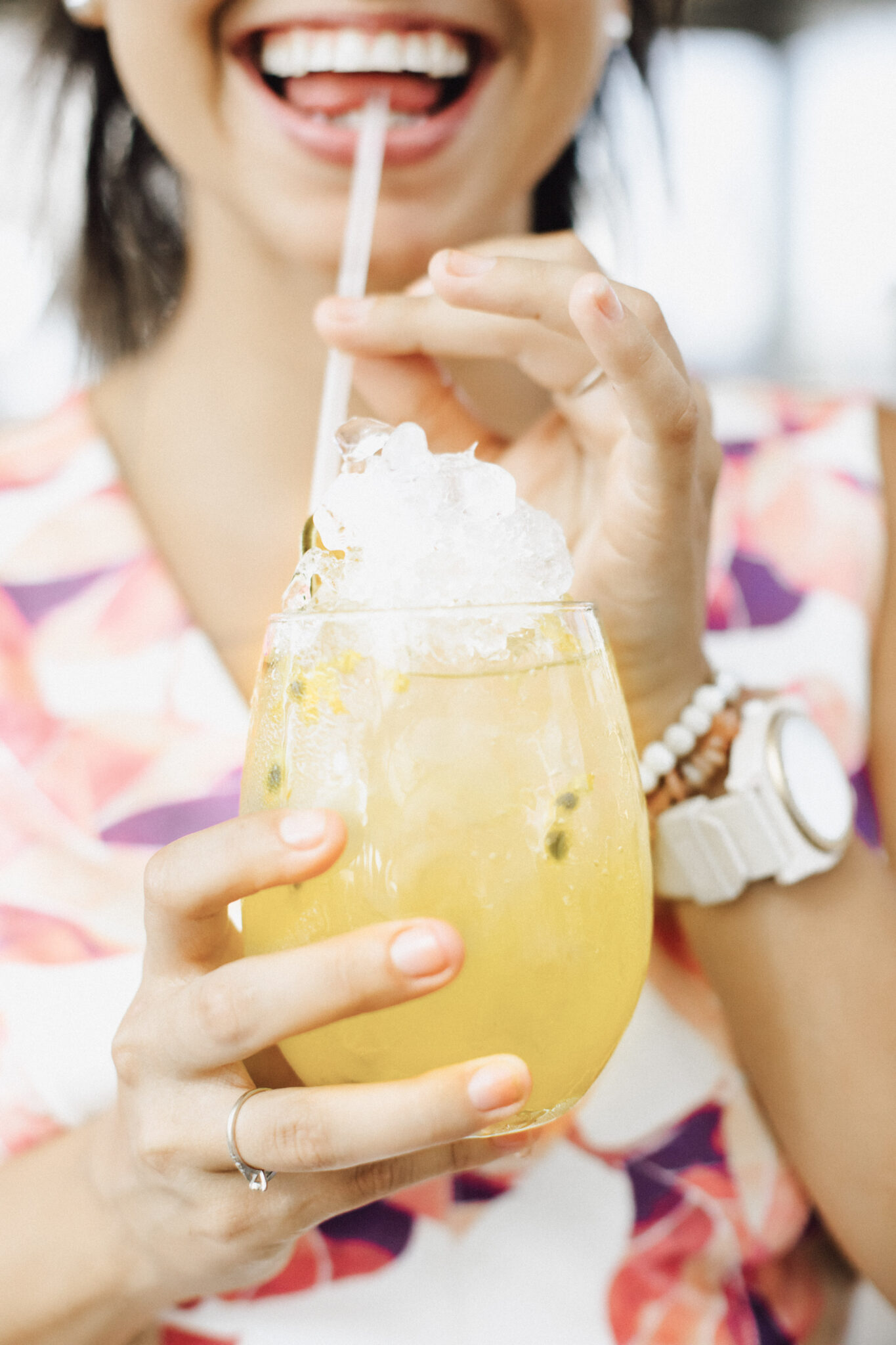 A woman's bottom half of her face is shown. She is smiling and holding a straw up to her mouth. She is drinking an orange cocktail with her pinky up. This article covers entertaining essentials every good host should have.
