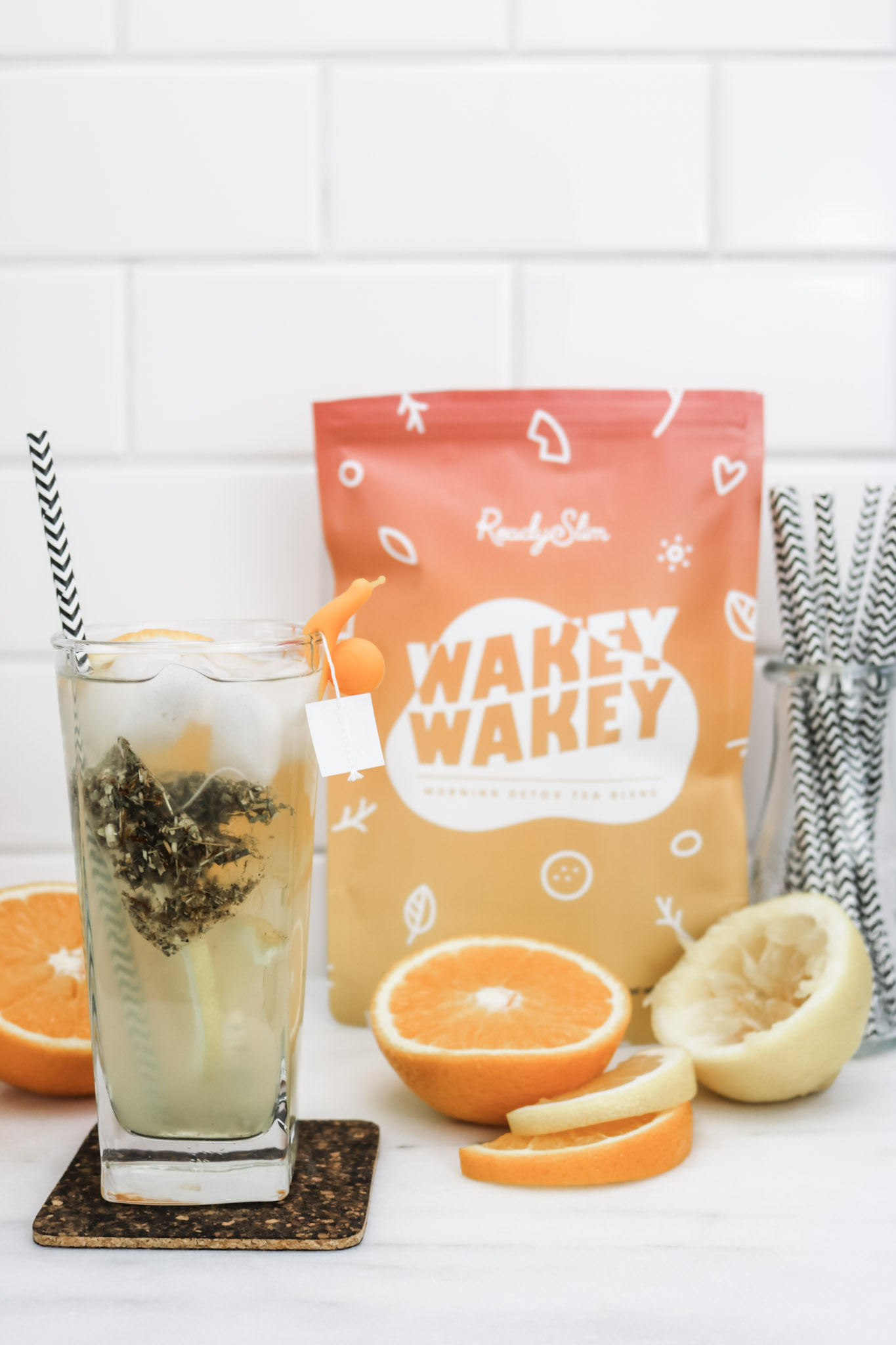 A tall glass of Wakey Wakey tea is shown with ingredients used to make it surrounding it. A bag of Wakey Wakey is behind it. 
