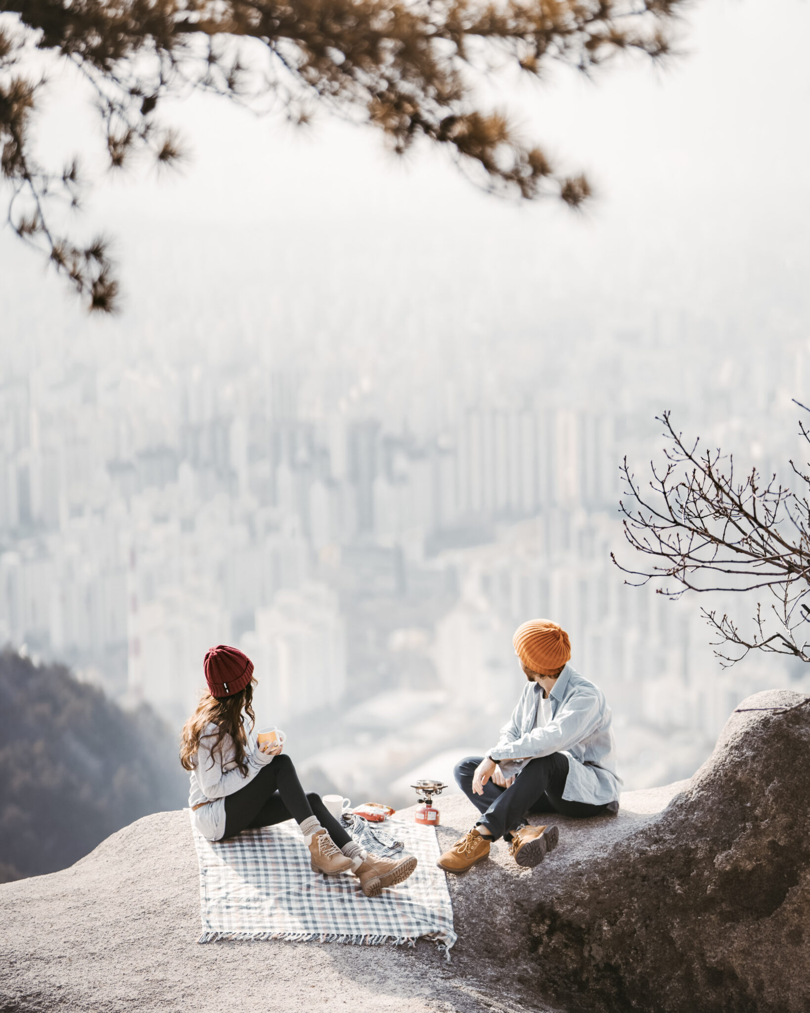A couple have a picnic on a rock overlooking a beautiful cityscape. This article covers how to cut the costs of your next travel adventure.