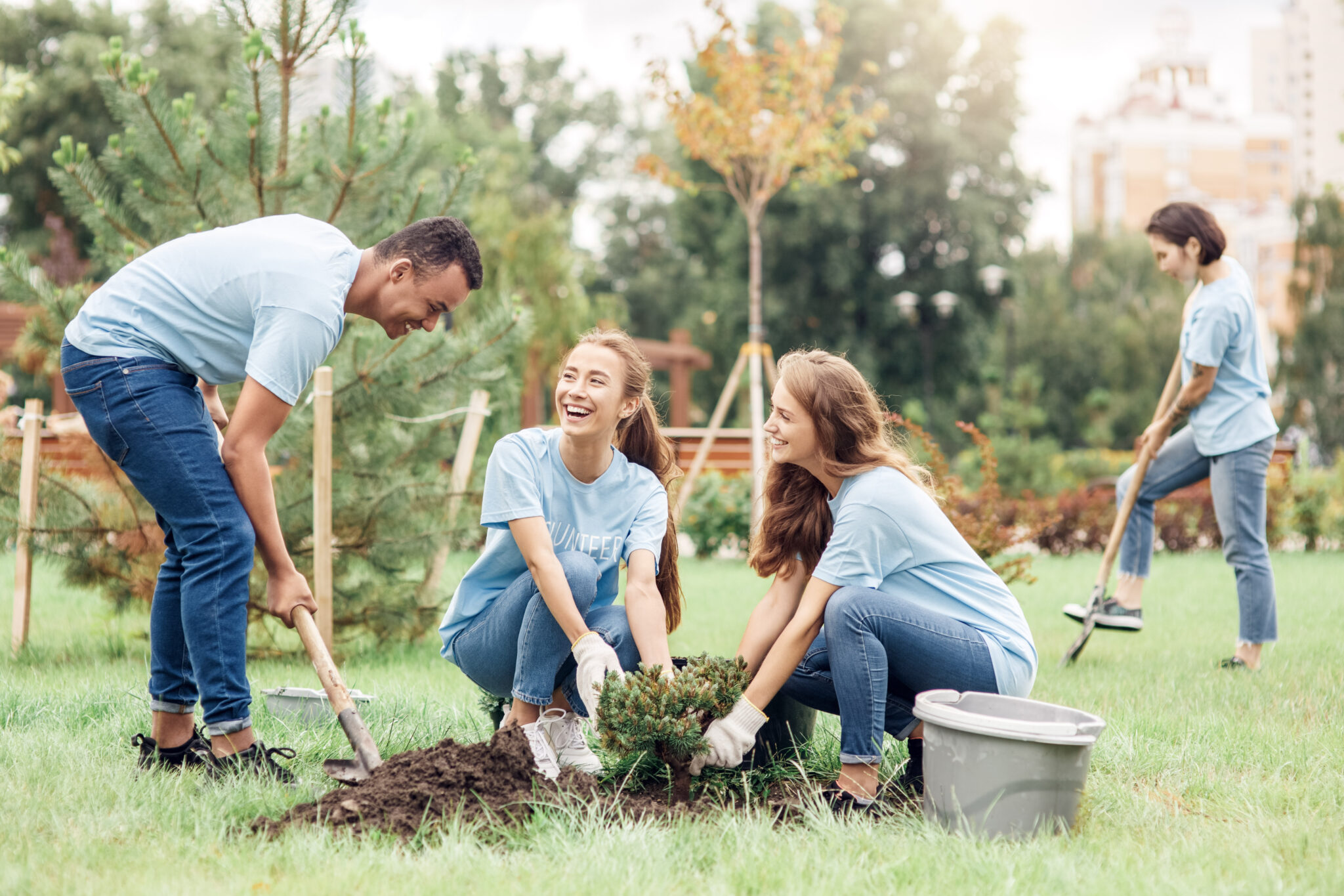Two women and a man plant a tree together. They look at each other and laugh. This article covers how to give back to your community.