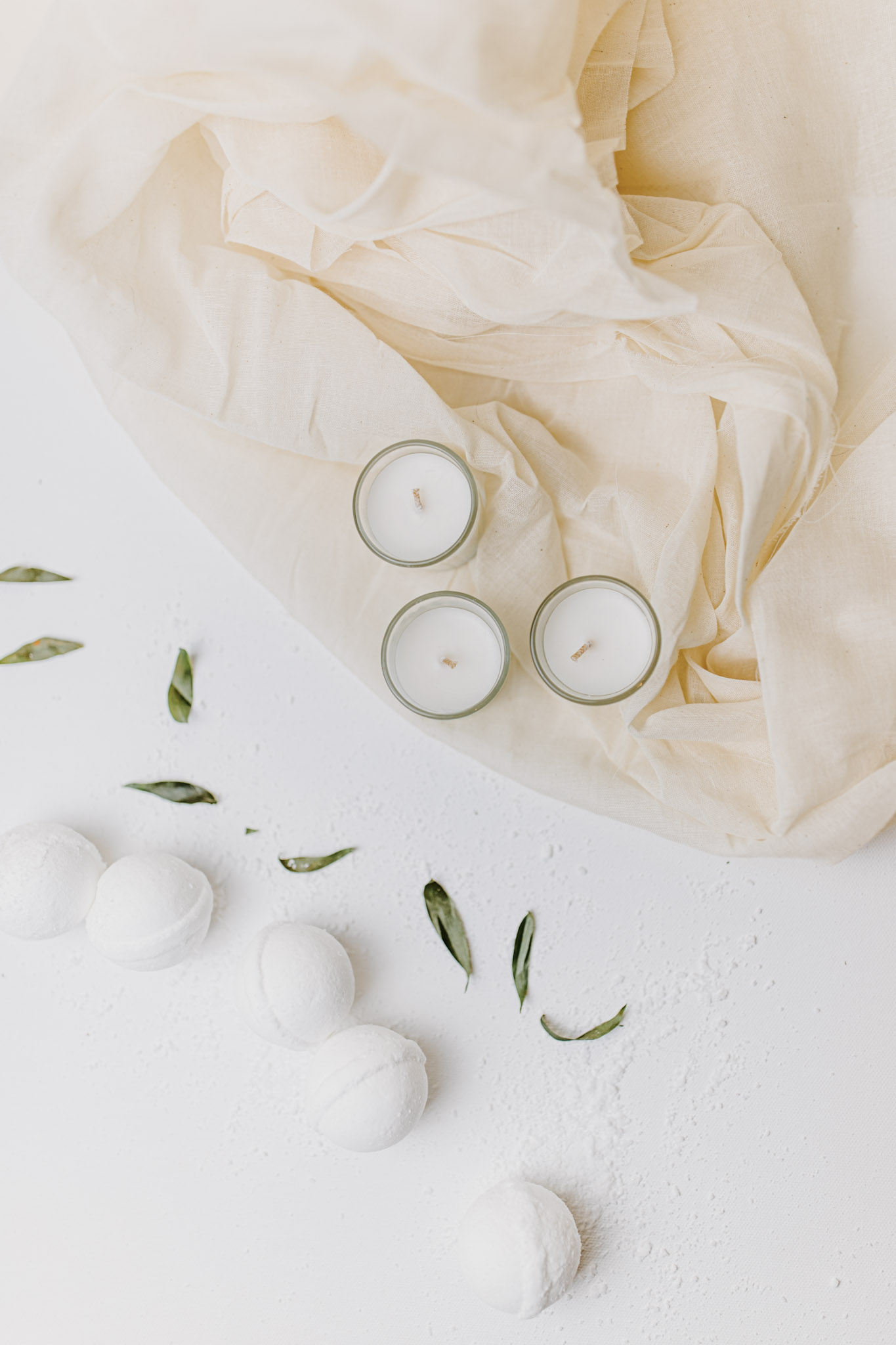 Candles and bath bombs are shown in a bathroom setting. There are leaves strewn around them. This article covers truths about CBD bombs.