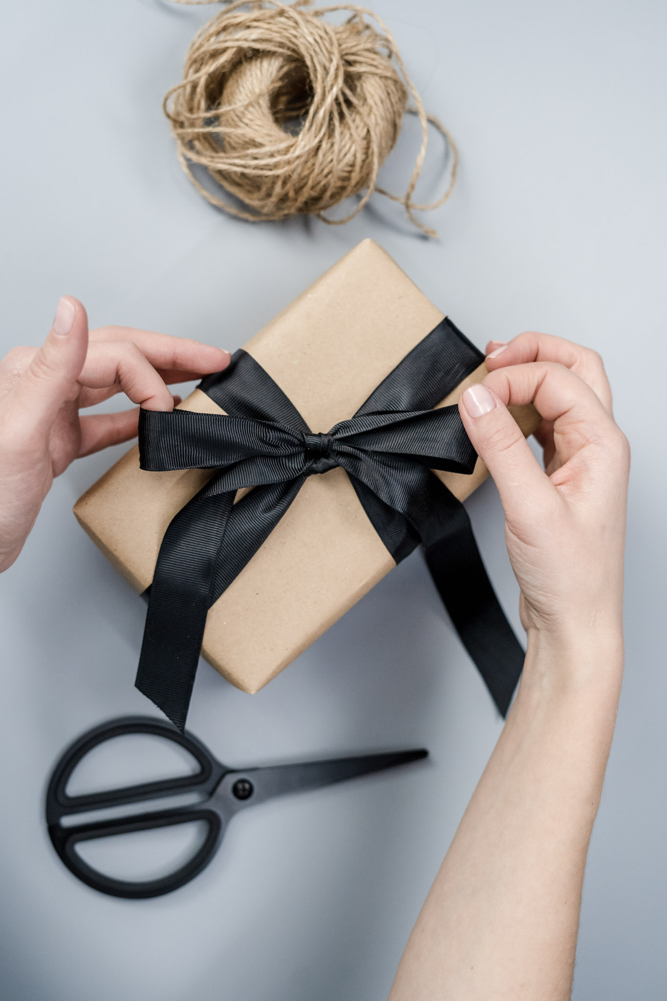 Hands are wrapping a bow on a present that is wrapped in butcher paper. This article covers how to make your Christmas more sustainable. 