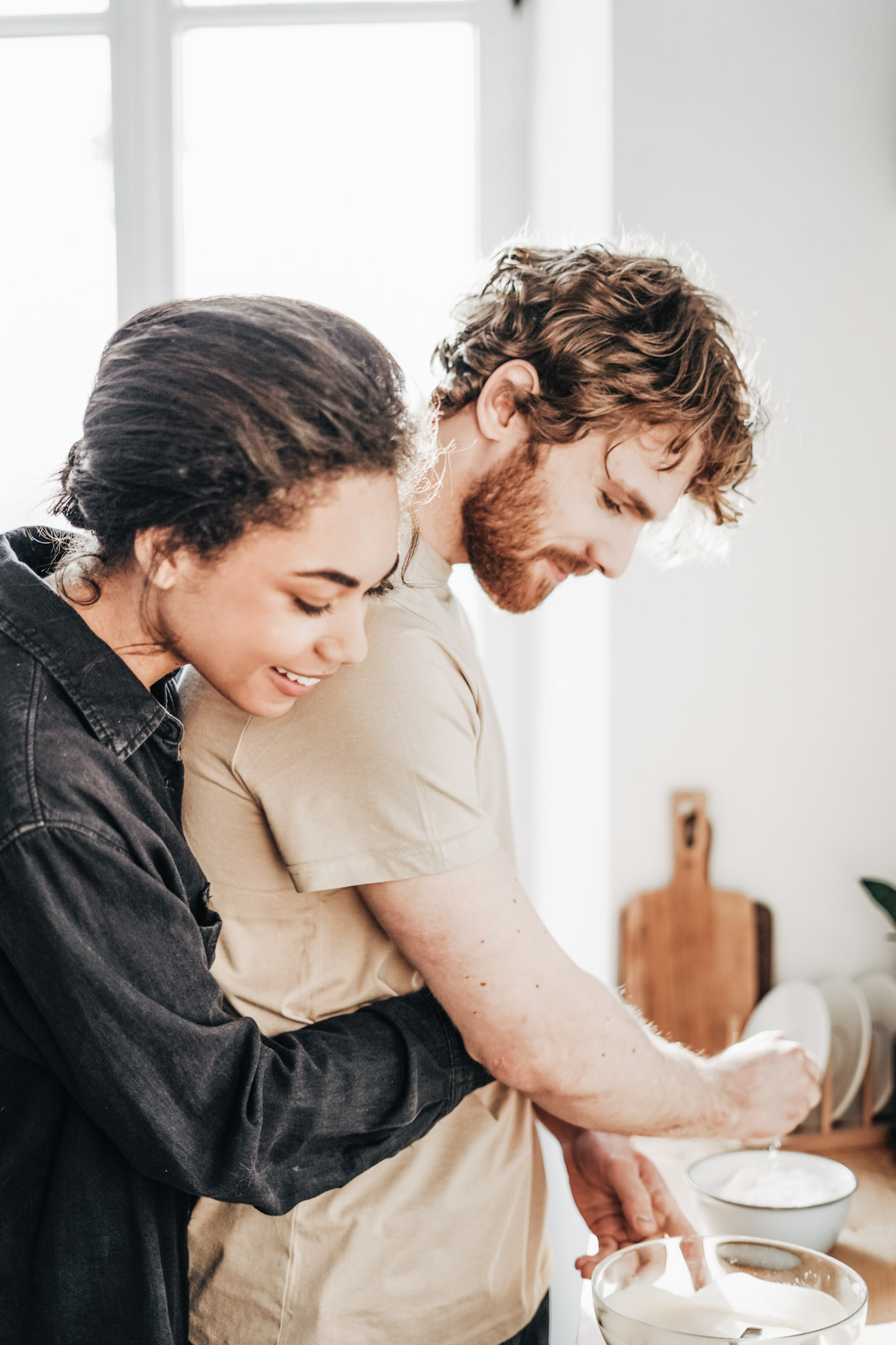 A woman and man embrace and cook together. The woman is hugging the man from behind while the man prepares food. This article covers romantic gourmet dinner ideas for a perfect Valentine's Day at home. 