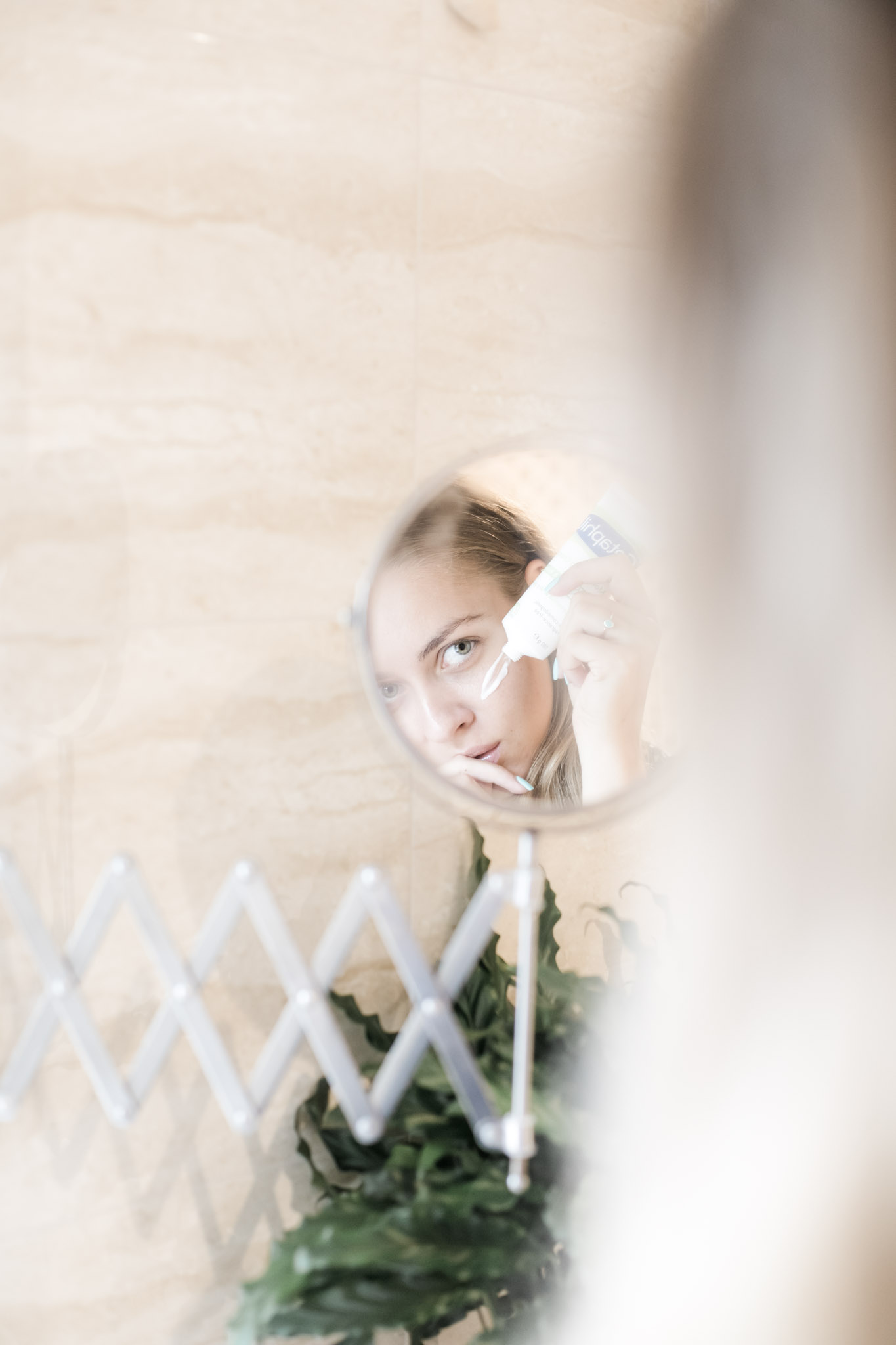A close up of a woman applying skin care product on face and looking in the mirror. This article covers what you need to know about protecting the health of your skin.