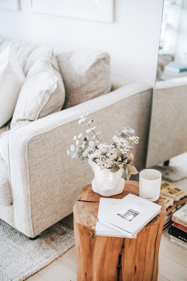 A tree stump is used as a table. There is a couch/sofa in a grey/beige. It is all beautifully styled with neutral decor and plants. This article covers the question: What Makes the Perfect Couch?