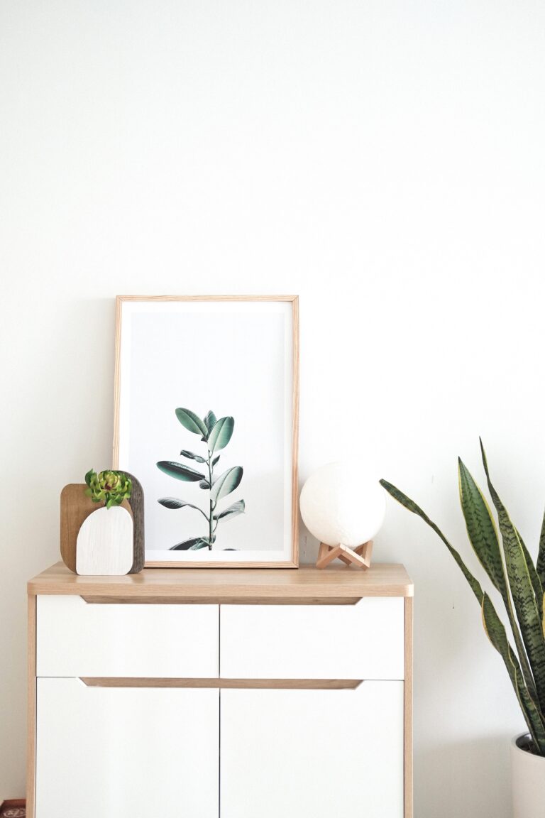 A console table with a plant and original artwork that matches the design of the room. This article covers how to select and style photos for modern living spaces.