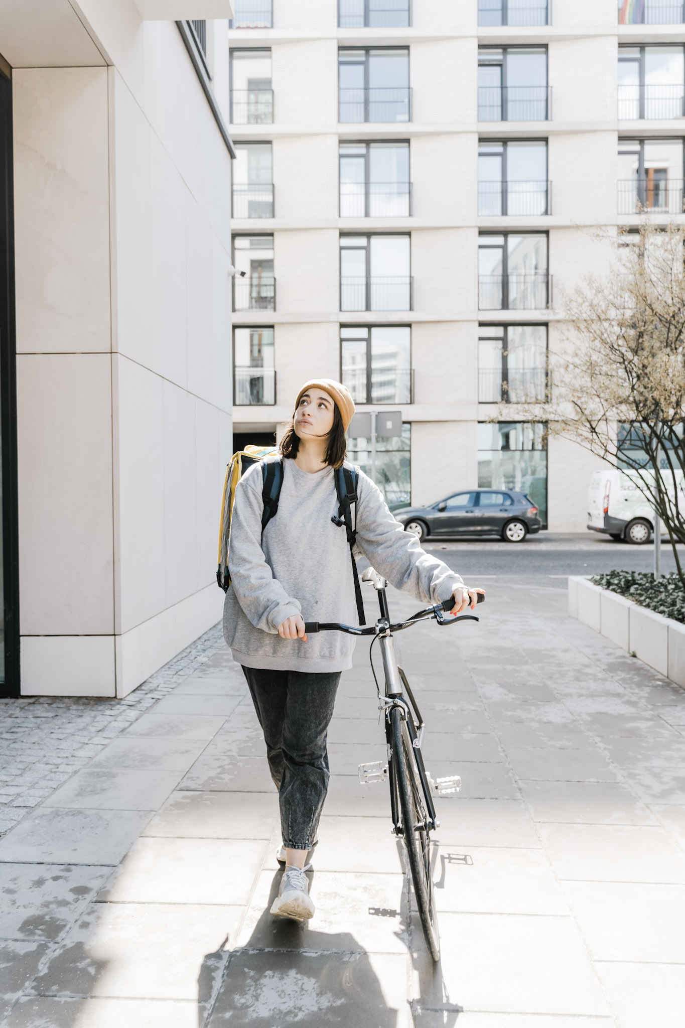 A girl casually walks through buildings while pushing a bicycle. The girl is looking up. This article covers 4 essential safety tips when riding a bicycle.