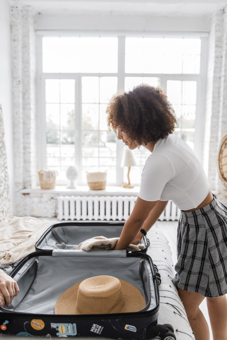 Woman with beautiful curly hair is in a room with a luggage on her bed and is packing for a trip. This article covers facts about extending luggage lifespan.