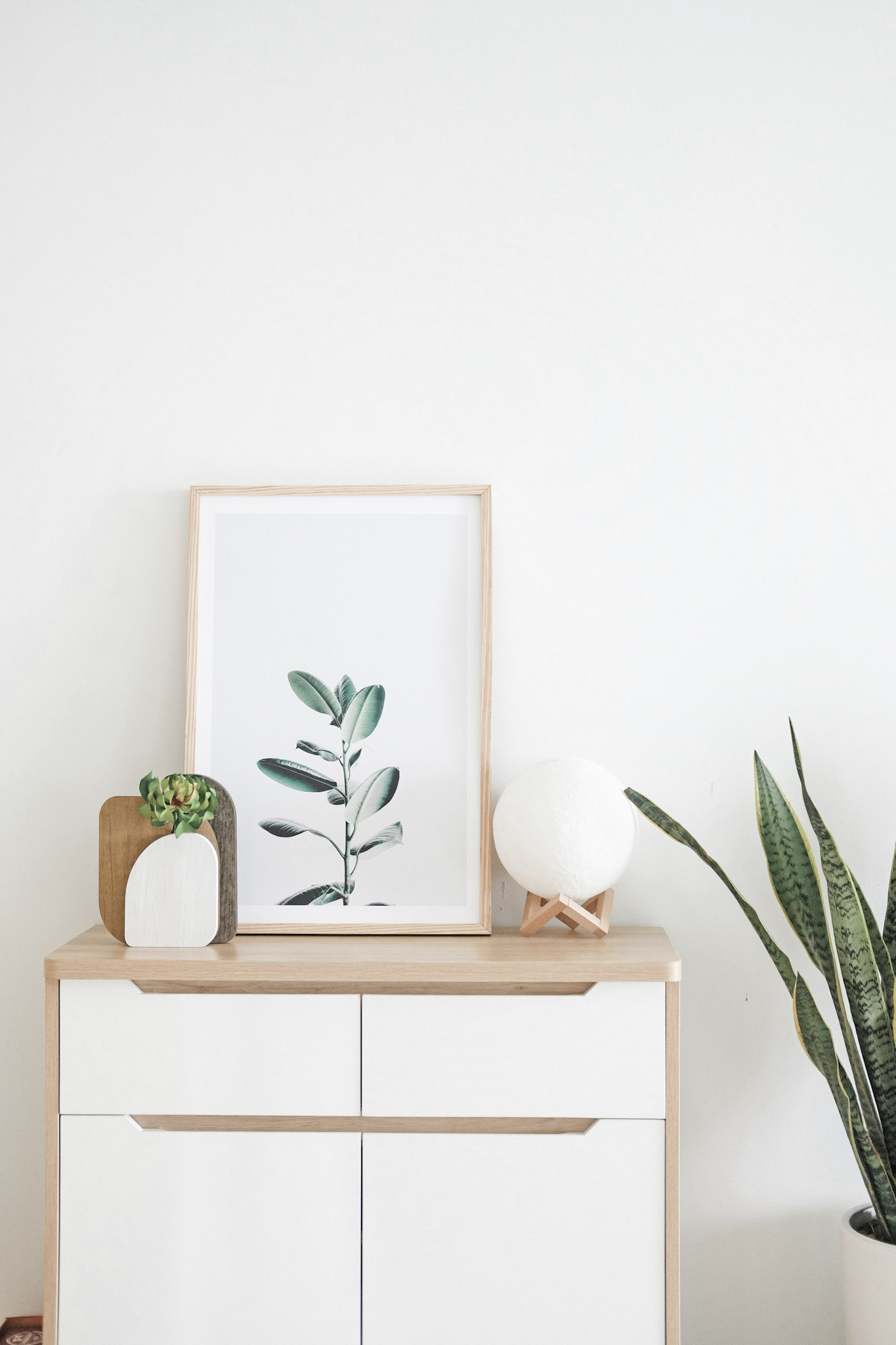 A white and natural wood night stand with wall art leaning. This article covers using wall art to infuse color and personality.