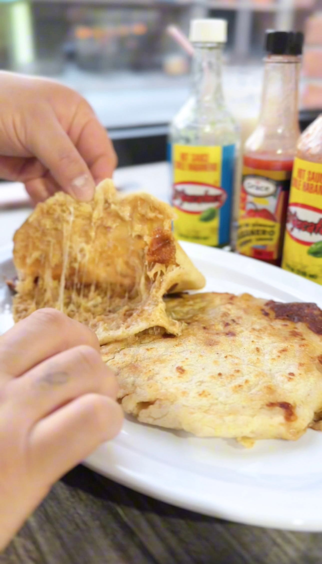 A person opens up a pupusa, to eat them the Salvadoran way.