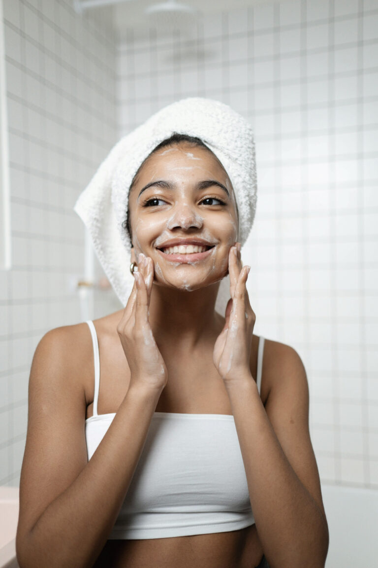 A beautiful woman with tanned skin wearing a towel on her head washes her face and smiles. This article covers things women are doing differently to look and feel younger.