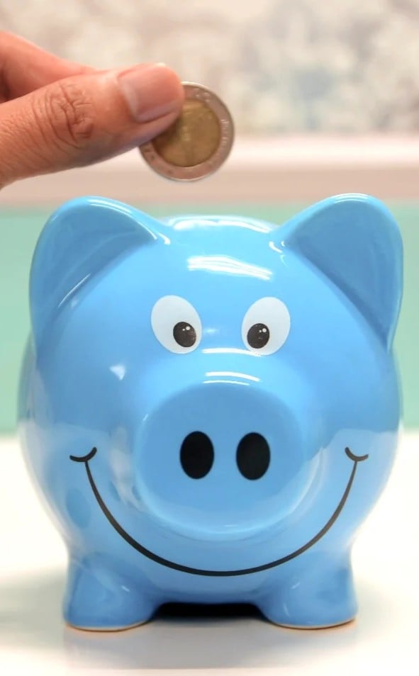 A woman inserts a coin into a blue piggy bank. This article covers how modern savers are thinking beyond traditional banks.