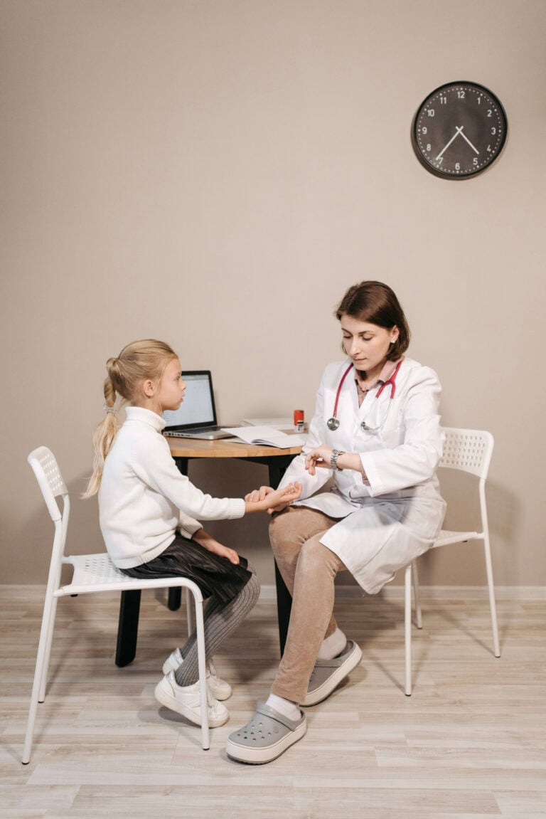 A small child sits with a doctor while she takes the child's blood pressure. It is a doctor's office setting. This article covers how to support your child's health.