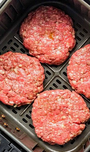 An air fryer with hamburger patties is shown. There are buns and cheese on the side. This article shares how to make the perfect air fryer hamburger.