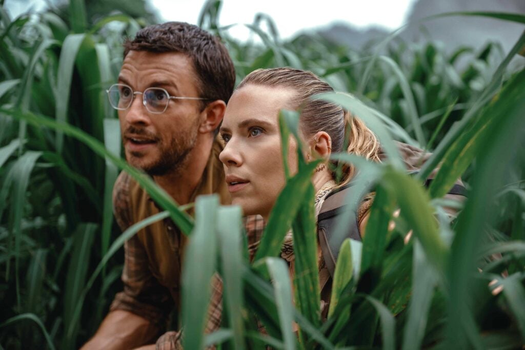 Scarlett Johansson and Jonathan Bailey hide in the brush and look intently at something that is out of sight. This article shares a Jurassic World: Rebirth review.