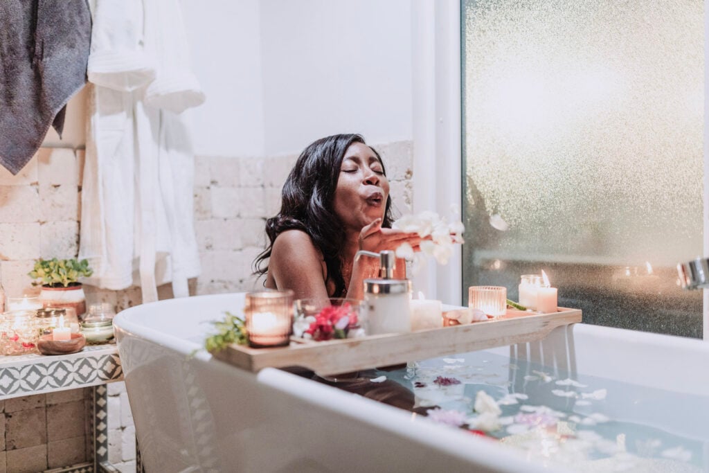 A woman blows bubbles in the tub and has a tray in front of her filled with self-care items. This article covers the self-care spaces you didn't know you needed.