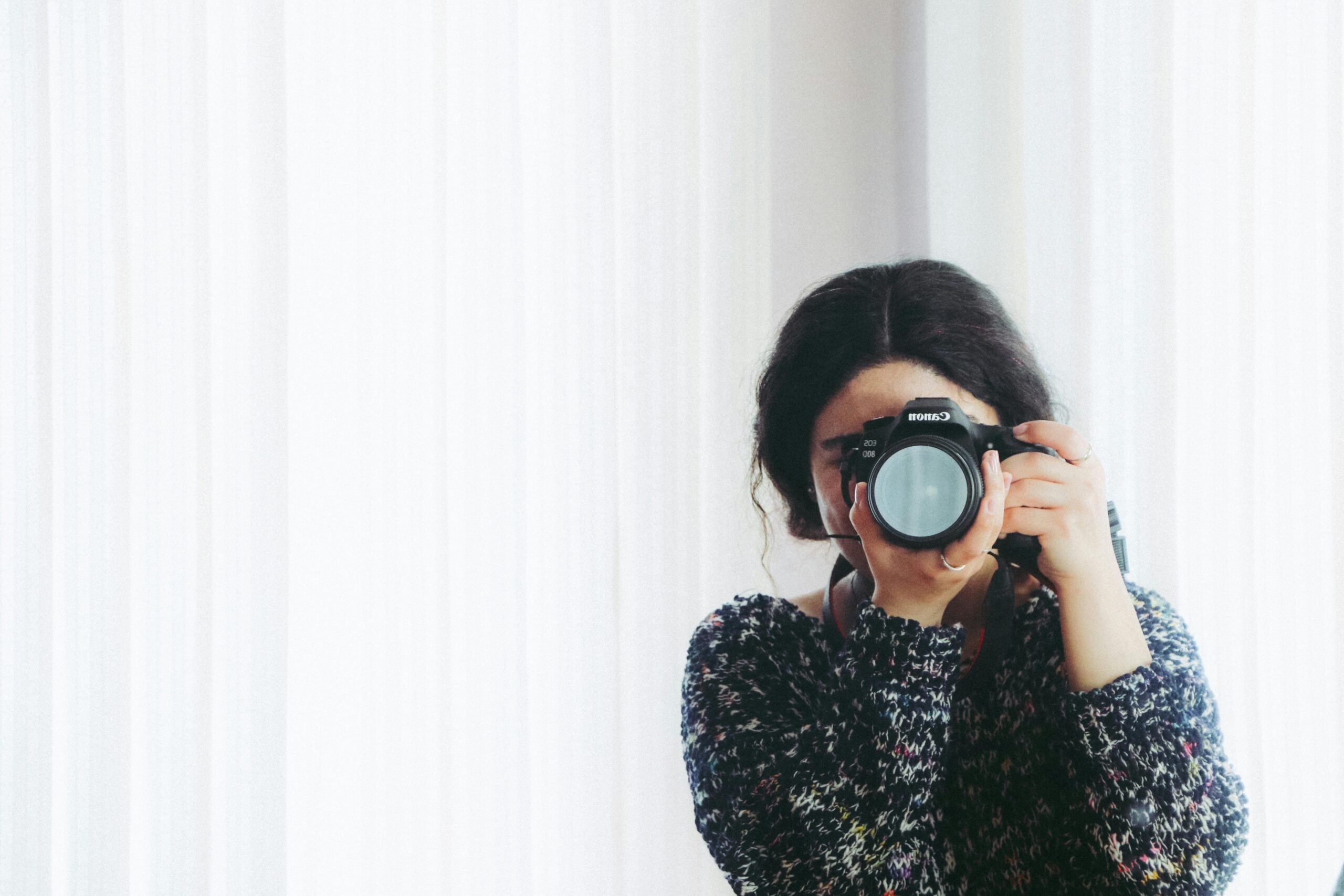 A woman holds a camera and points it back to the camera. This article covers turning trips into treasured moments.