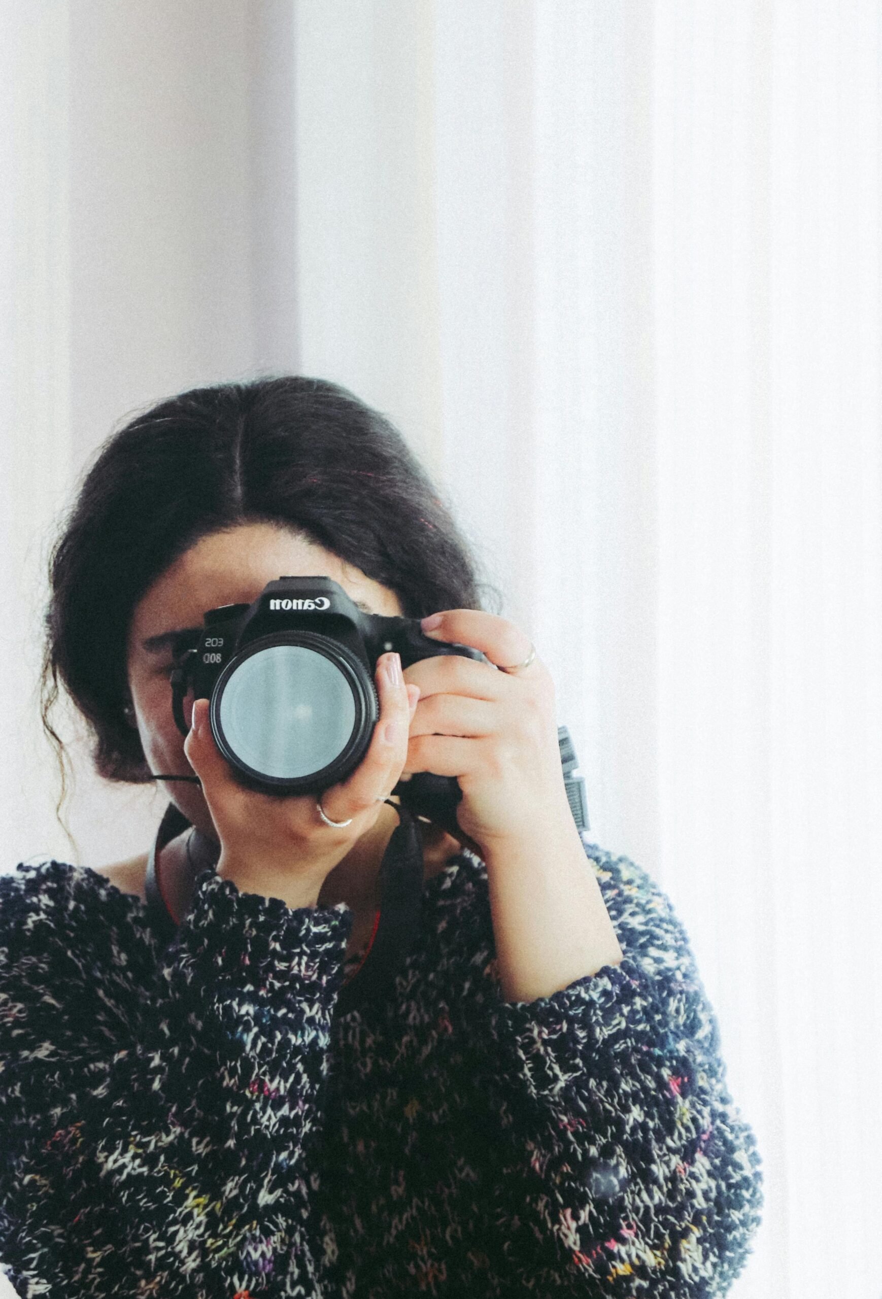 A woman holds a camera and points it back to the camera. This article covers turning trips into treasured moments.