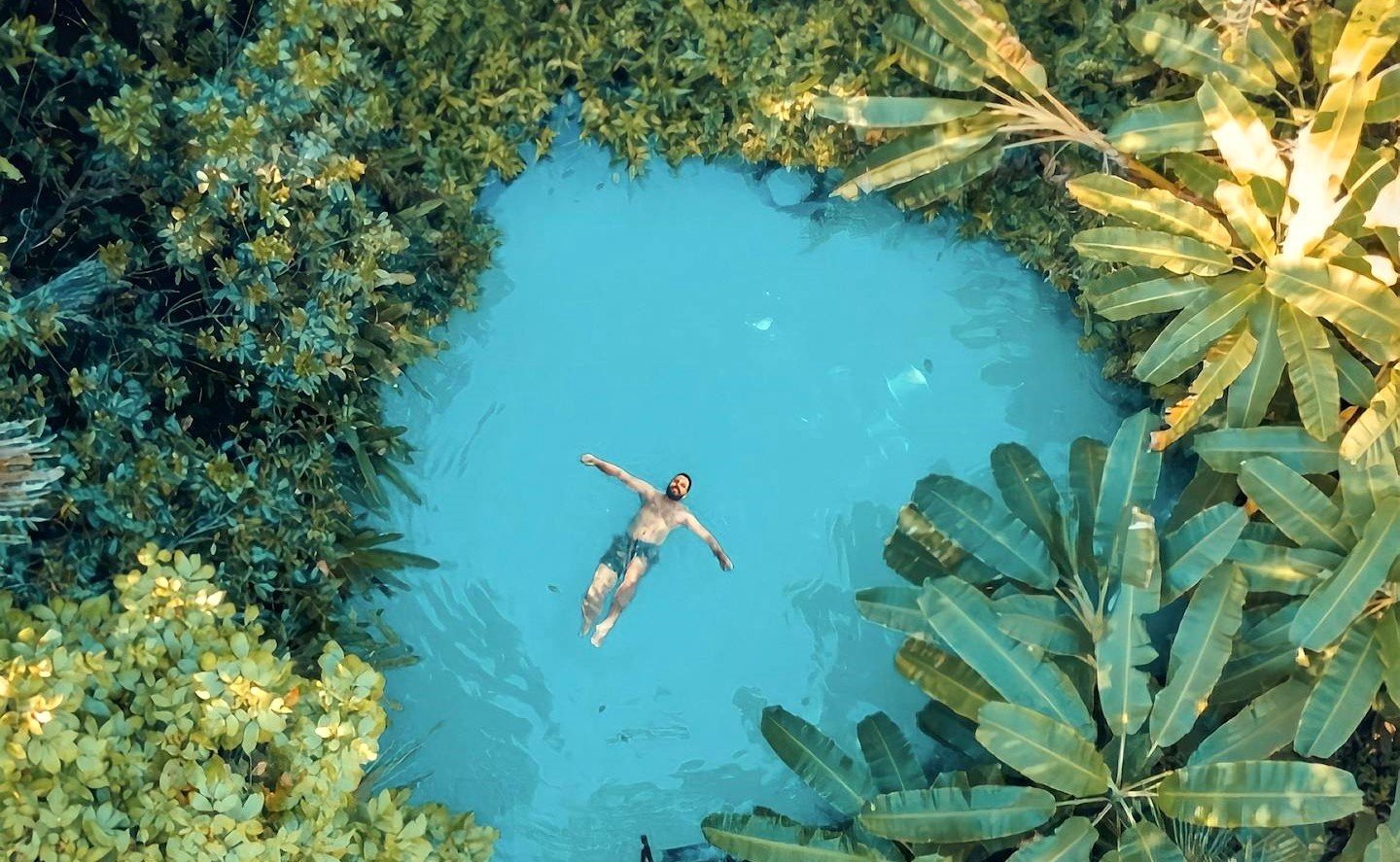 Aerial view of a man swimming in a serene tropical lagoon surrounded by lush greenery. This article covers solo safety trips every explorer should know.