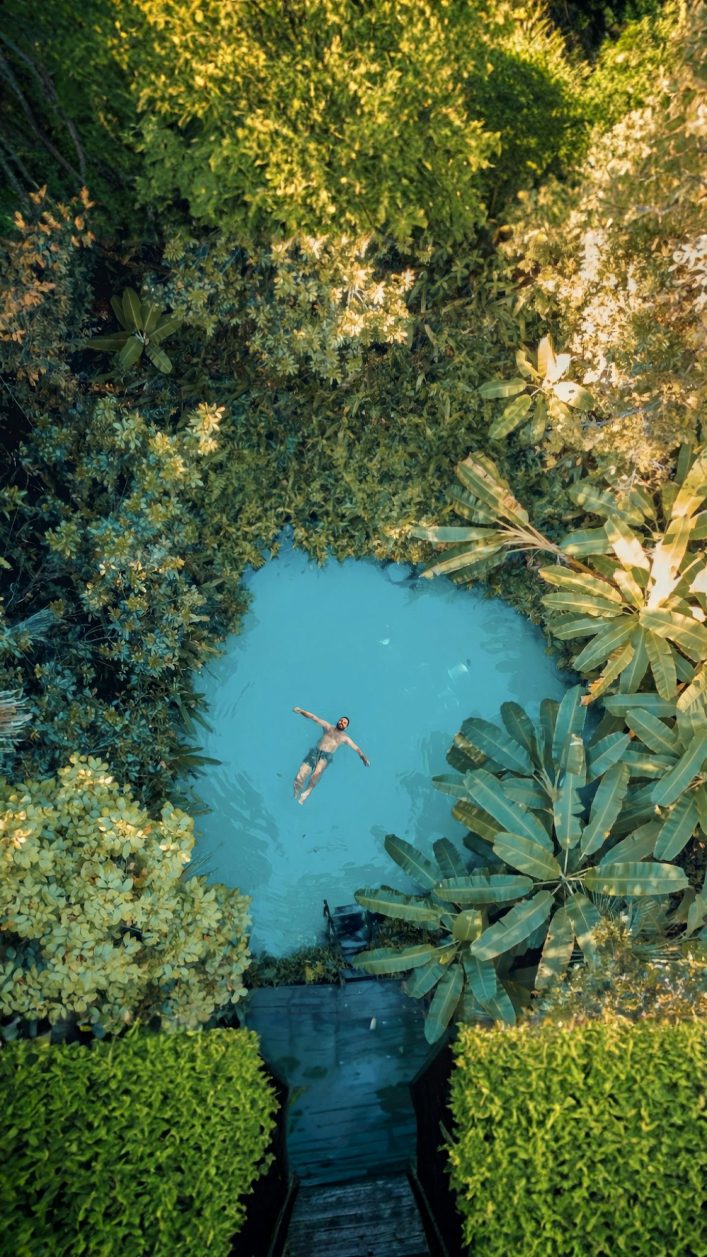 Aerial view of a man swimming in a serene tropical lagoon surrounded by lush greenery. This article covers solo safety trips every explorer should know.