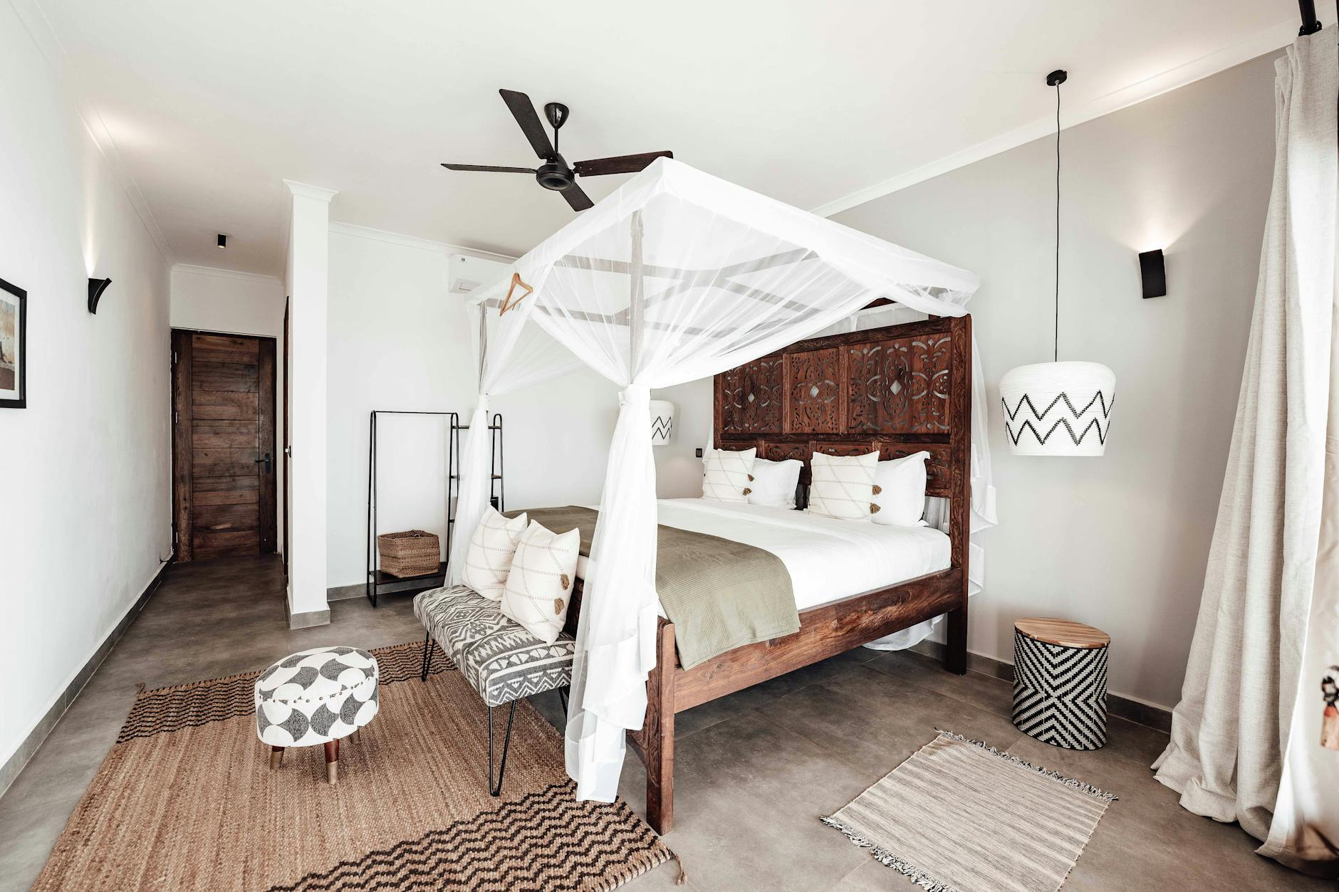 A wooden carved bed with white canopy and rugs in a bedroom. This article covers bedroom ceiling fan ideas.