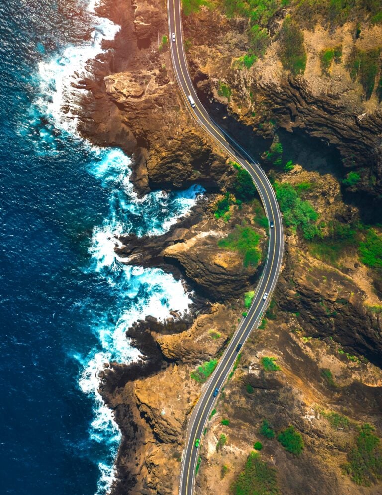 A bird's eye view of Hawaii. Cars drive down a road that winds the shoreline. This post covers how to plan a calm Hawaiian escape.