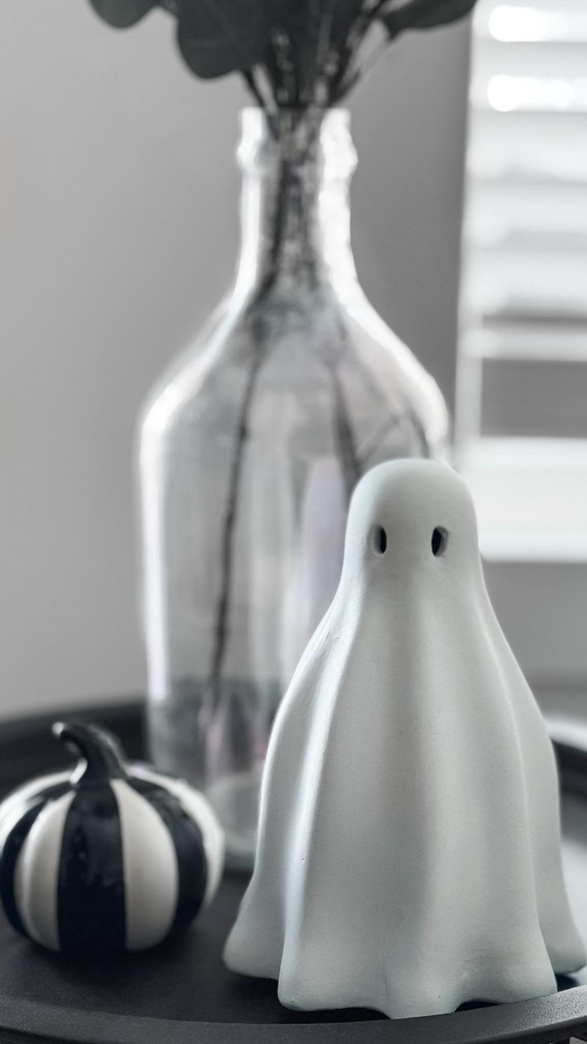 A vintage ghost and black and while pumpkin sit on a black round table with a vase with eucalyptus vines.