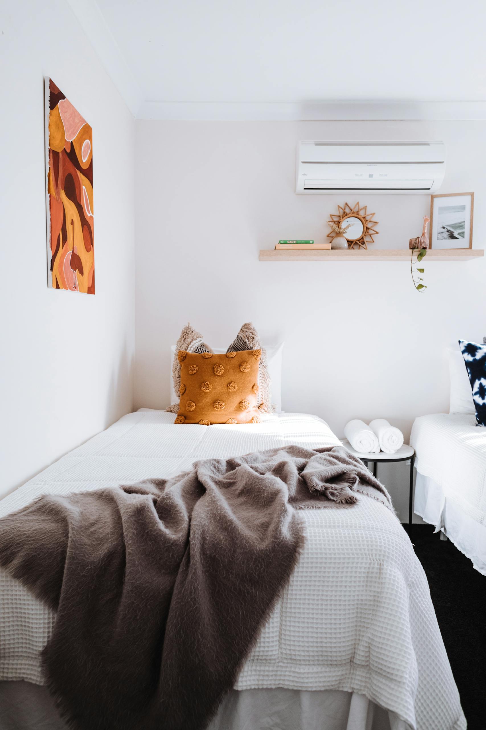 A minimalist bedroom featuring a single bed with soft textures, warm decor, and modern design. This article covers air conditioner installation costs and benefits.