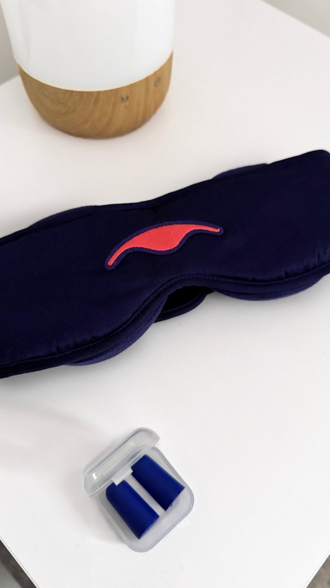 Manta Silk Sleep Mask on a bedside table with a diffuser and earplugs.