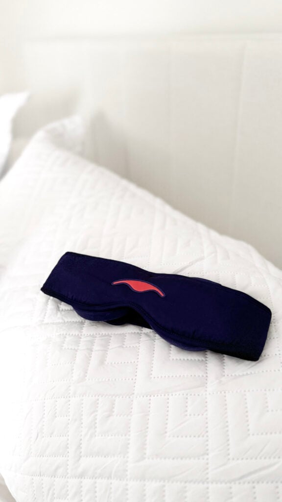 Manta Silk Sleep Mask resting on a white pillow in a bed.