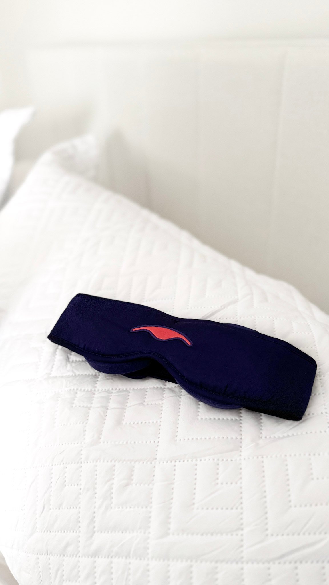 Manta Silk Sleep Mask resting on a white pillow in a bed.