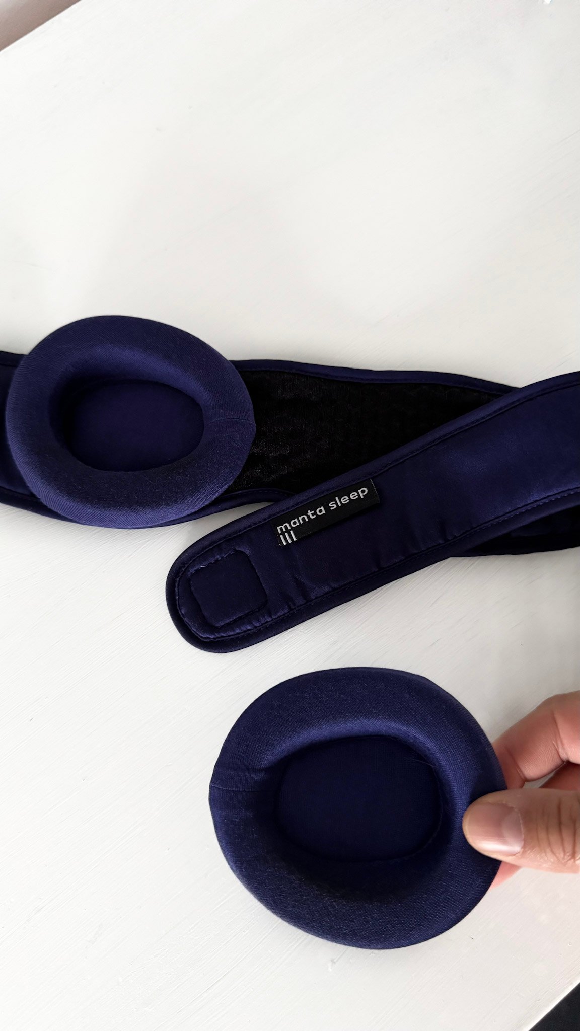 Manta Sleep Silk Mask eye cups, that are padded. A hand holds one that is detached.