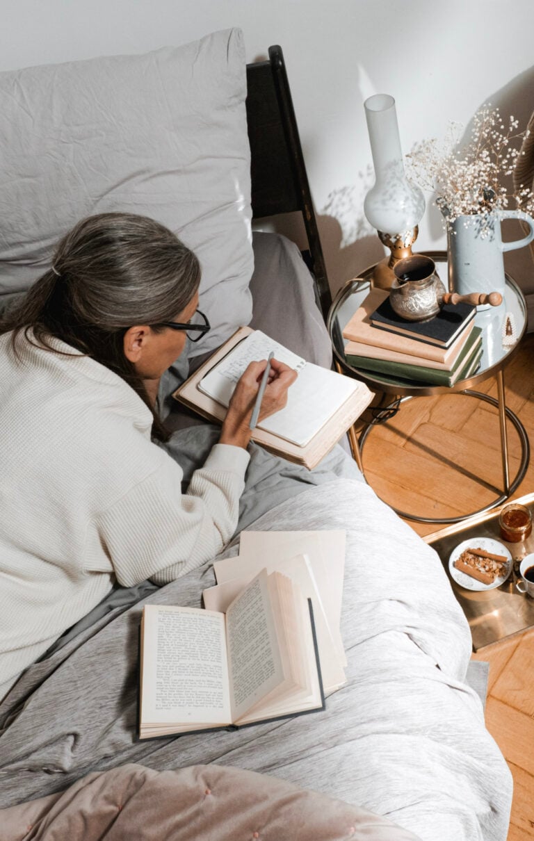 Woman lays on her bed, journaling. Her room is comfy and cozy. This article covers how different parts of your home work together to keep you comfortable.