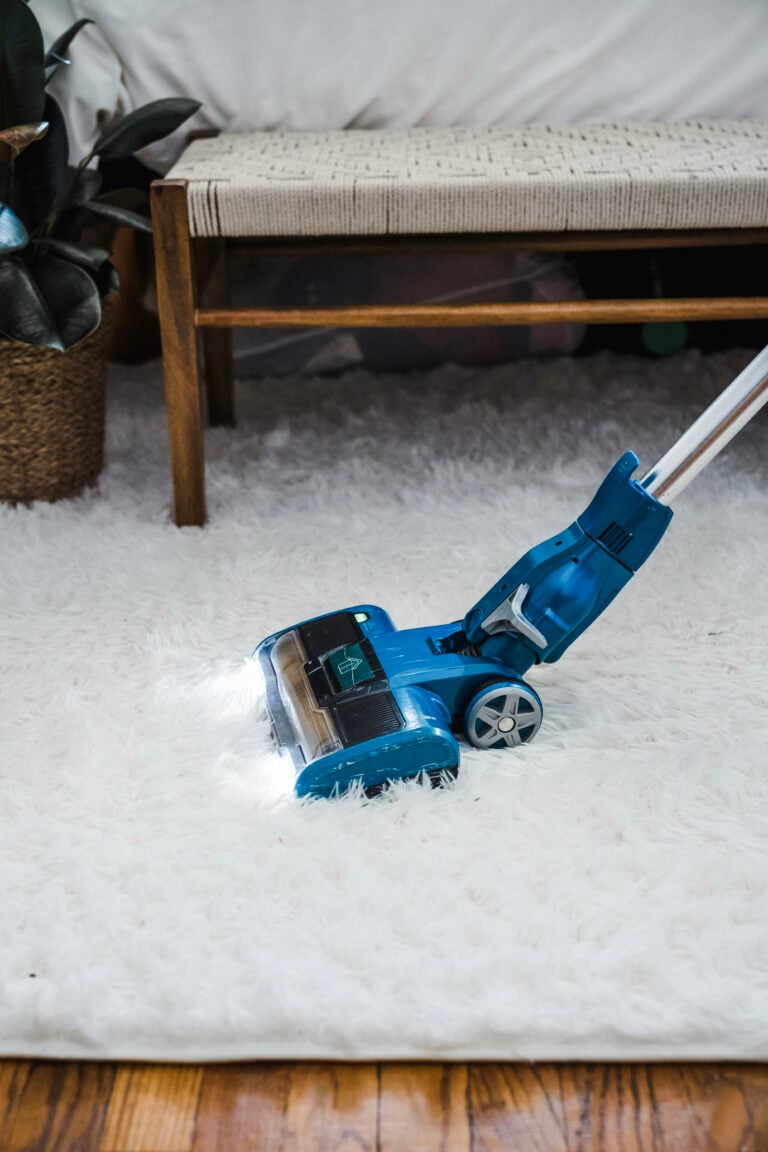 Vacuum cleaning a white carpet in a room. This article covers overlooked home maintenance tasks that make a big difference.