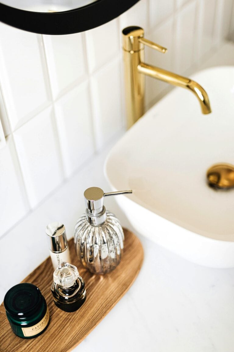 A modern bathroom with a gold faucet and a round black mirror are shown. This article covers bathroom renovation trends for modern homes.