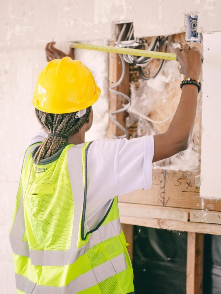 A woman measures an insulated wall. This article covers the role of insulation in reducing house costs.