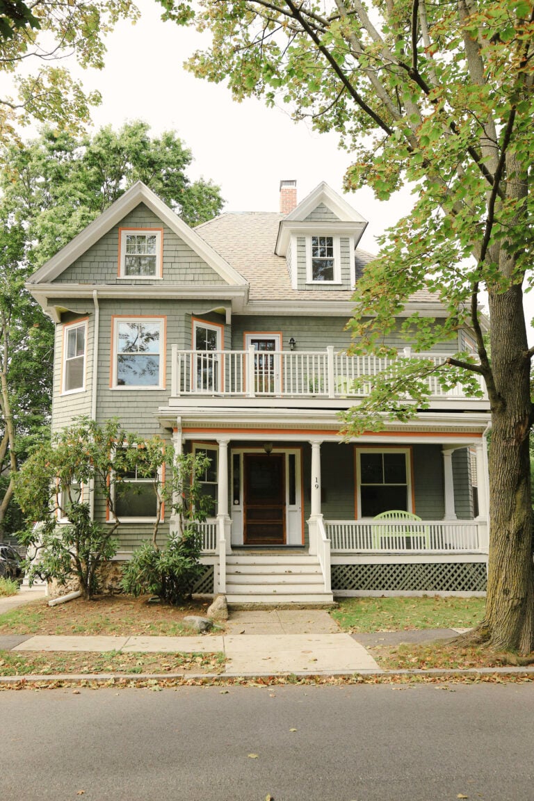A beautiful two-storey house is shown with mature trees in front. This article covers seasonal home maintenance tips every home owner should know.